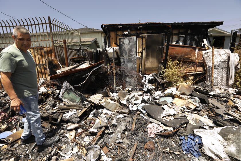 WATTS, CA - JUNE 14, 2022 - - Gustavo Flores stands behind his home that was damaged in a recent fire caused by a homeless encampment that settled behind his house along 108th Street in Watts on June 14, 2022. Flores and his family moved to a nearby apartment where they not only have to pay rent, but have to continue paying the mortgage on their fire damaged home. Many homeowners and businesses in the area worry about the continued presence of homeless living in the area and the continued trouble and challenges they bring to the neighborhood. (Genaro Molina / Los Angeles Times)