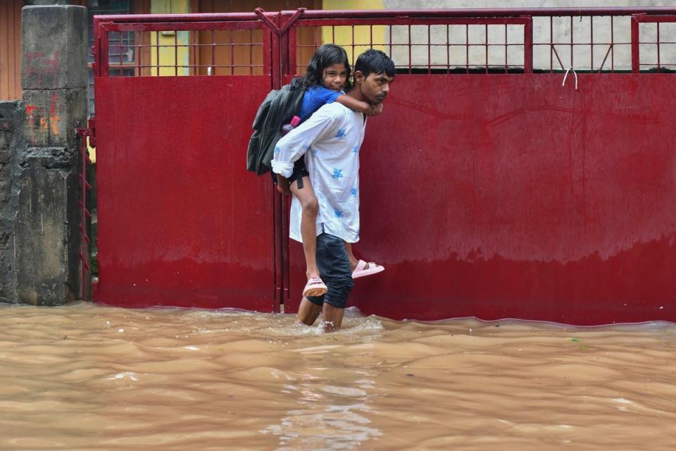 A man carries his daughter on back as he wades through a flooded street in Guwahati on June 20 (AFP via Getty Images)