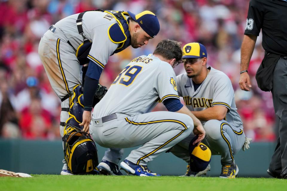 Brewers catcher Victor Caratin and shortstop Willy Adames check on starting pitcher Corbin Burnes, who was feeling the affects of the heat and humidity in Cincinnati during the fifth inning.