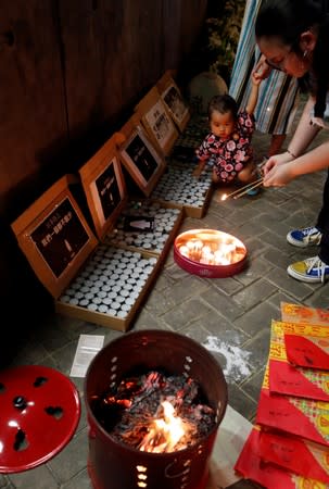 A child observes a woman holding incense sticks as people gather at Lennon Wall at Admiralty district during the Mid-Autumn Festival, in Hong Kong