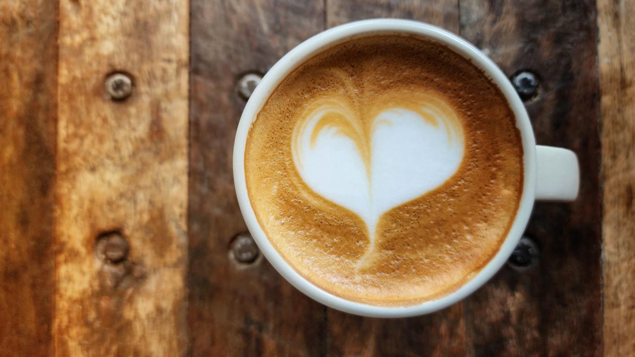 Heart-shaped latte art coffee in a ceramic coffee mug placed on a wooden table with copy space