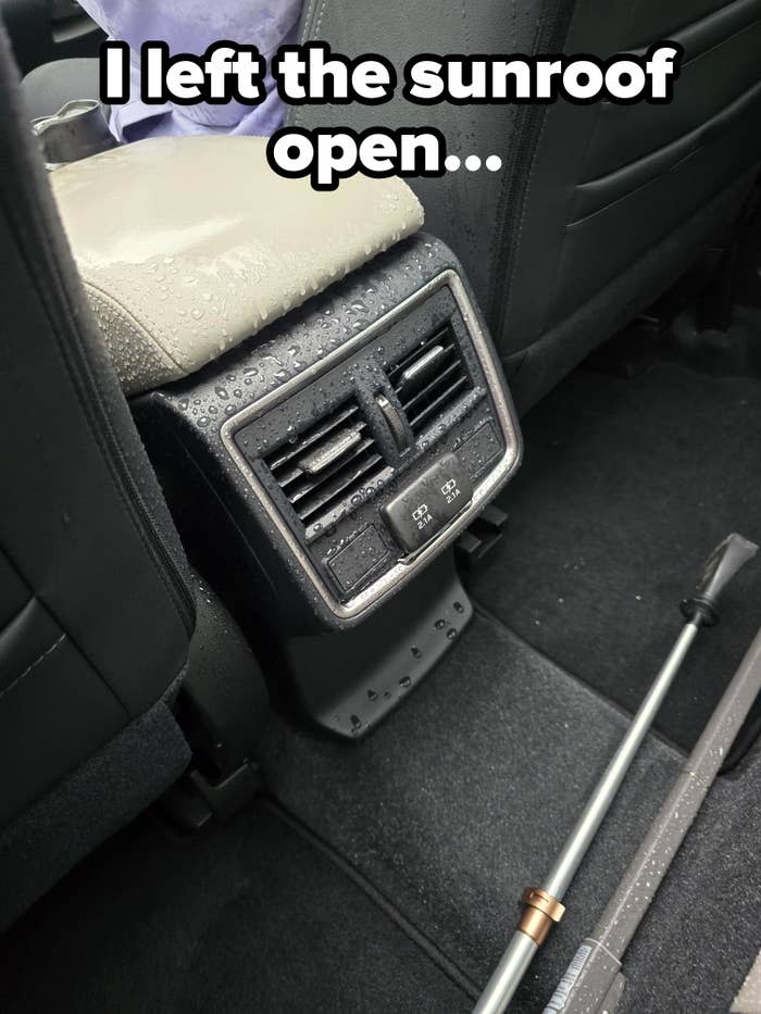 Backseat view of a car's air conditioning vents with water droplets on the armrest and a partially visible cane in the foreground