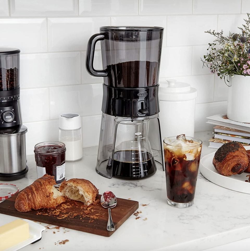 OXO Good Grips Cold Brew Coffee Maker on kitchen counter near iced coffee and croissant (photo via Amazon)