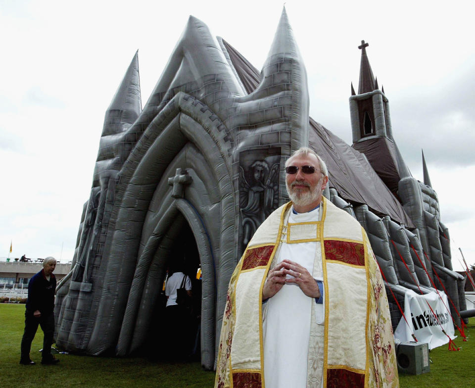 Father Michael Elfred, a church minister from Tadworth, Surrey stands outside the world's first inflatable church which has been erected May 13, 2003 in Sandown, England. The church stands 47ft tall from floor to steeple, comes complete with inflatable organ, candles and stained glass windows, and can hold up to 60 people. Father Michael later performed a service a dedication for the church. (Photo by Hugo Philpott/Getty Images)