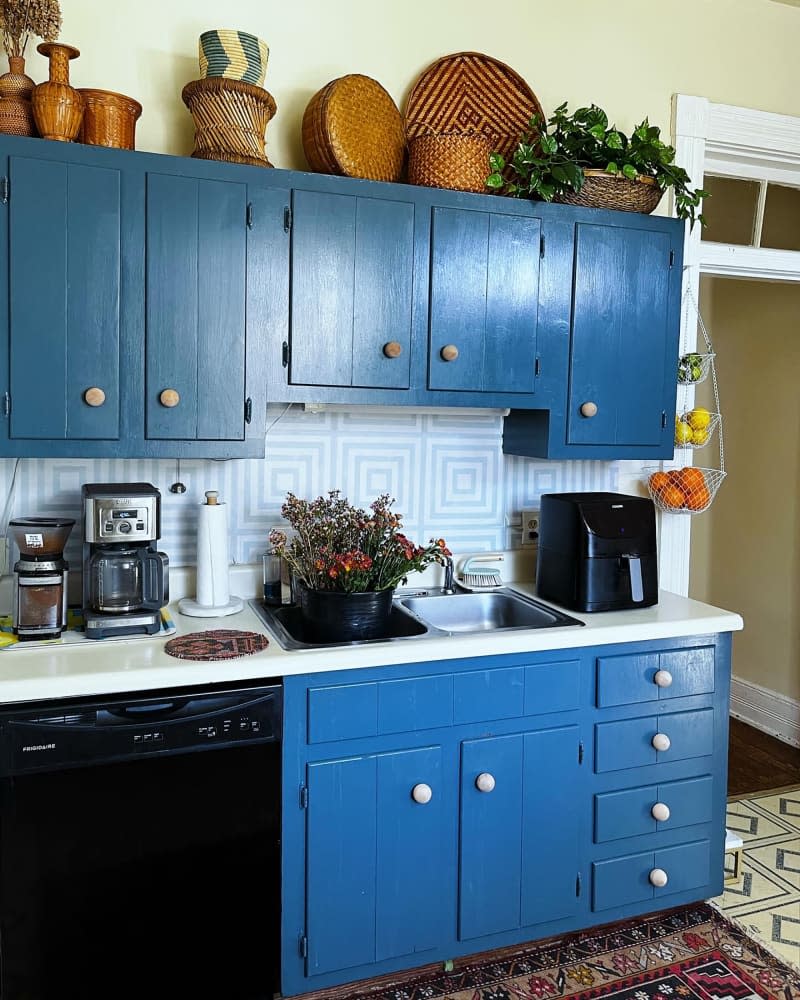 Wood and rattan decor atop blue cabinetry in pale yellow kitchen with graphic backsplash and tile.