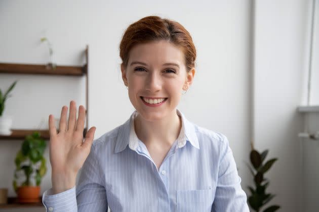 Head shot portrait of attractive smiling businesswoman waving hand, looking at camera, making video call with webcam, greeting, business coach recording video for vlog, saying hello (Photo: fizkes via Getty Images)