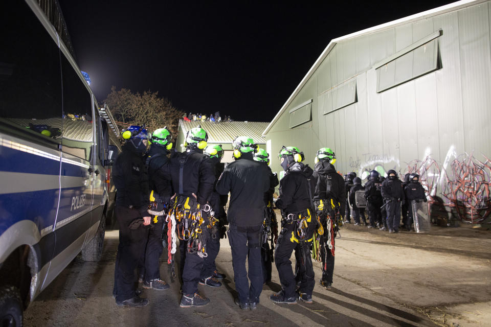 Climate activists sit on the roof of a barn, in the foreground high-altitude climbers of the police stand together for a situation briefing, in Luetzerath, Germany, Wednesday, Jan. 11, 2023. Environmental activists have been locked in a standoff with police who started eviction operations on Wednesday in the hamlet of Luetzerath, west of Cologne, that's due to be bulldozed for the expansion of a nearby lignite mine. (Thomas Banneyer/dpa via AP)