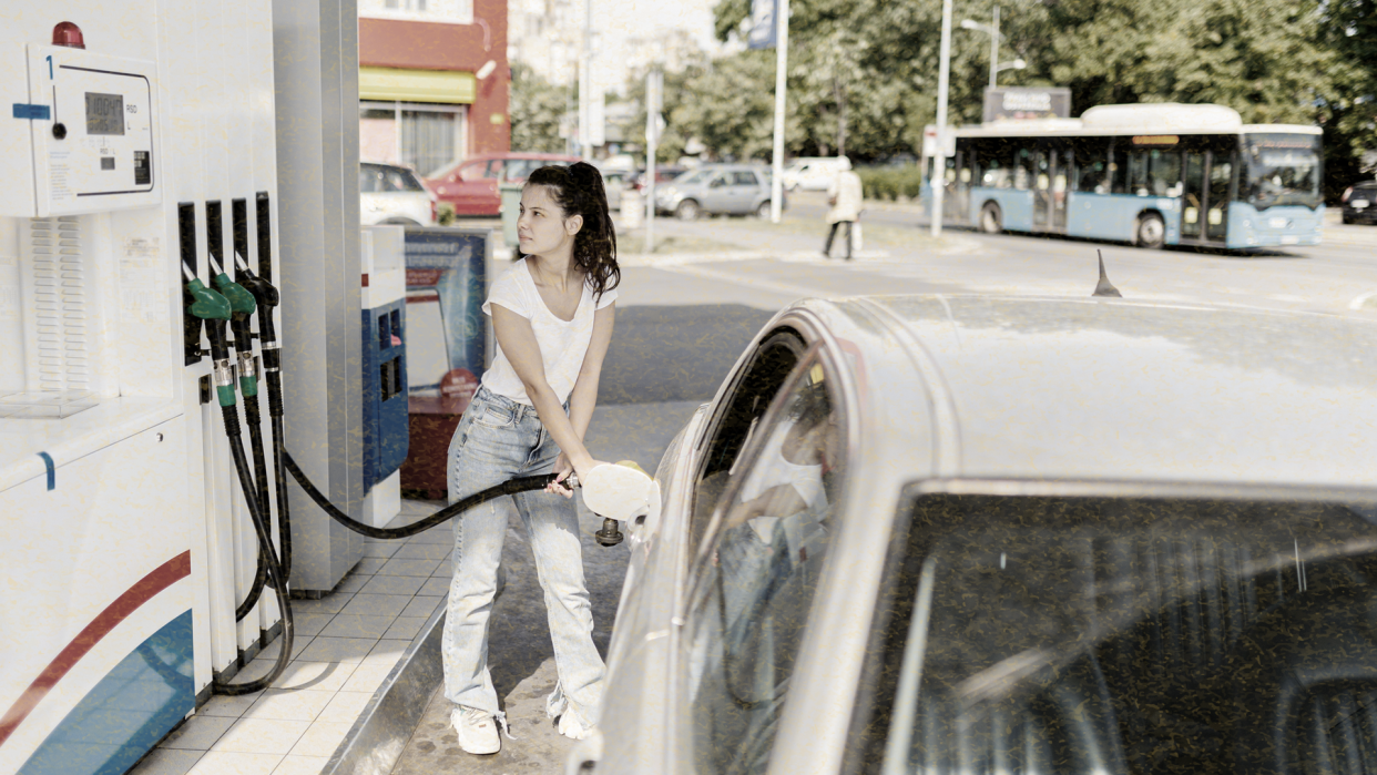 a person standing at a gas station filling up their tank