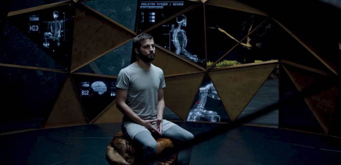 A man sits in a futuristic room, observing his experimental microchip surgery in “Upgrade”