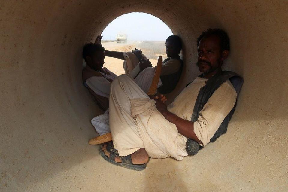 Three people shelter from the sun inside a cement pipe.