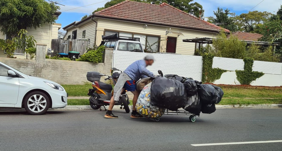 A photo of a man in Sydney's Northern Beaches pushing a trolley with 9 or more garbage bags with cans in them to seemingly be recycled through Return and Earn. Source: 2GB