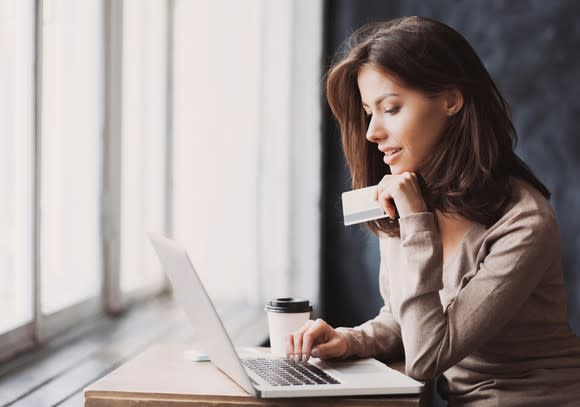 Woman sitting at table, using a computer and holding a credit card.