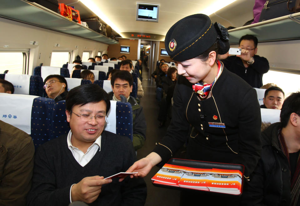 A conductor gives out a booklet to a passenger on the high speed train that runs on the new 2,298-kilometre (1,425-mile) line between Beijing and Guangzhou at a train station in Zhengzhou, central China's Henan province on December 26, 2012. China started service on December 26 on the world's longest high-speed rail route, the latest milestone in the country's rapid and -- sometimes troubled -- super fast rail network. The opening of this new line means passengers will be whisked from the capital to the southern commercial hub in just eight hours, compared with the 22 hours previously required. CHINA OUT AFP PHOTO