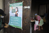 FILE - In this July 21, 2020 file photo, a city health department worker hangs a poster describing the guidelines for businesses operating during the coronavirus pandemic, as a woman prepares to make tortillas inside a small business, in San Mateo Xalpa in the Xochimilco district of Mexico City. Mexican health officials have been holding daily televised news conferences about the pandemic for months, but they have given mixed messages on the necessity of wearing a mask. (AP Photo/Rebecca Blackwell, File)