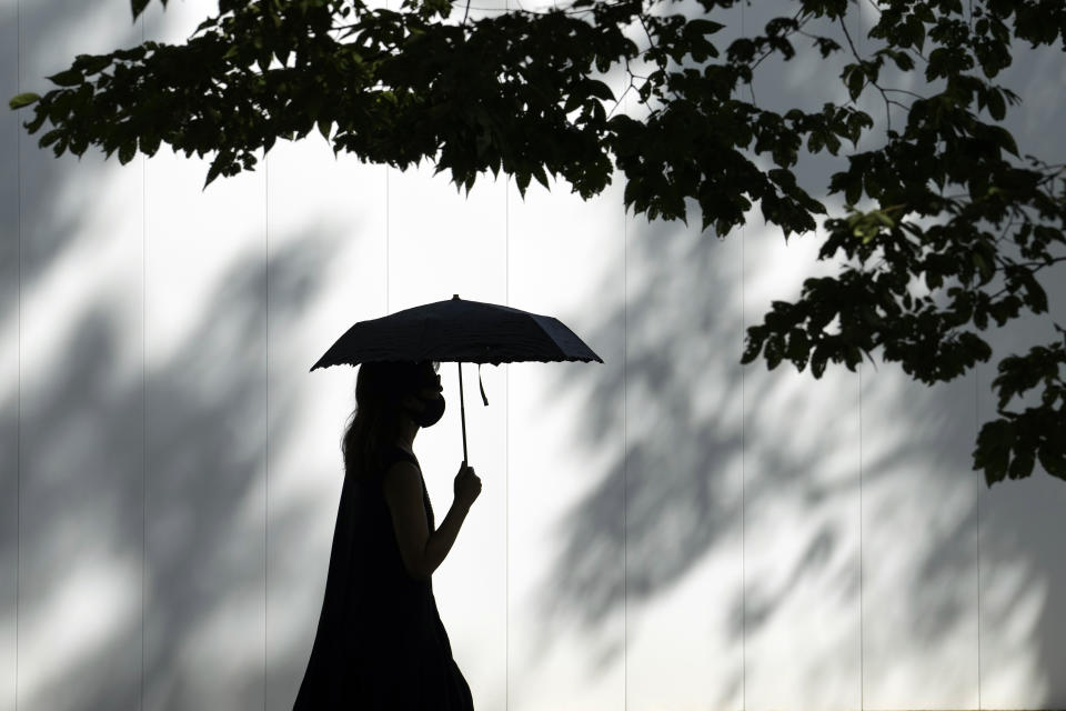 A woman wearing a face mask to help protect against the spread of the coronavirus walks under the scorching sun Wednesday, Aug. 11, 2021, in Tokyo, Japan. (AP Photo/Eugene Hoshiko)