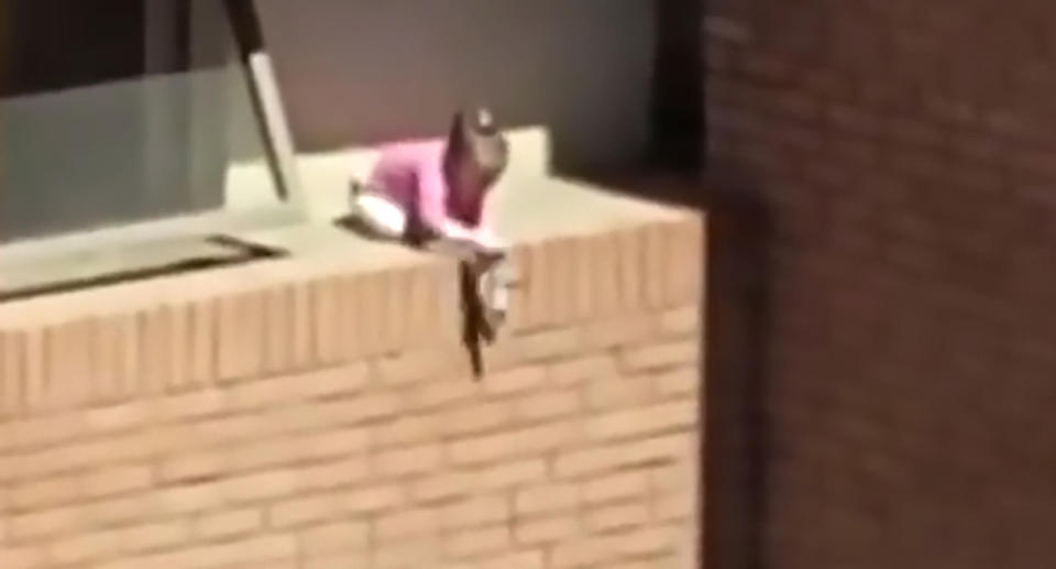 A toddler is seen playing with doll on a high-rise apartment ledge in Chile.