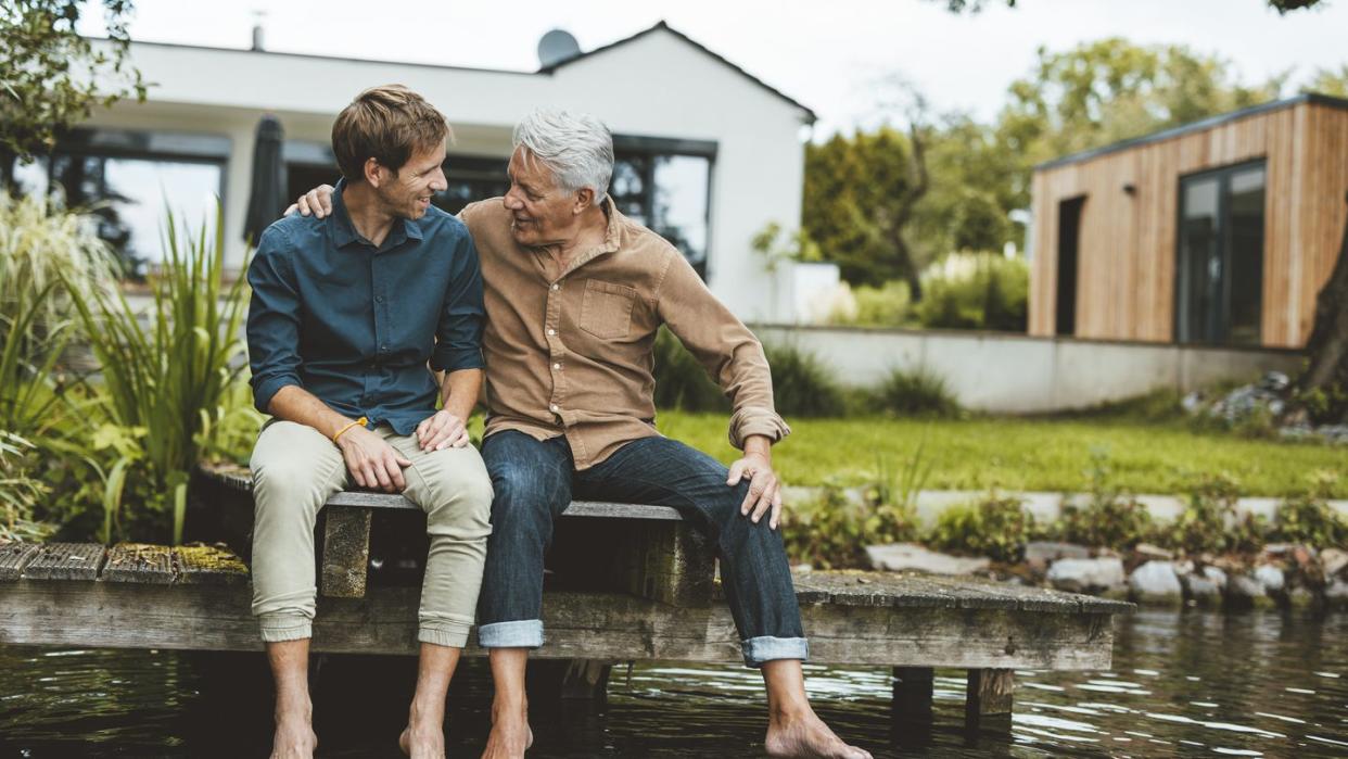 man talking with adult son sitting by lake in backyard