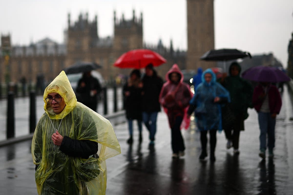 Tourists shelter from the rain as they walk over Westminster Bridge, with the Houses of Parliament in the background, in London on March 10, 2024. (Photo by HENRY NICHOLLS / AFP) (Photo by HENRY NICHOLLS/AFP via Getty Images) (AFP via Getty Images)