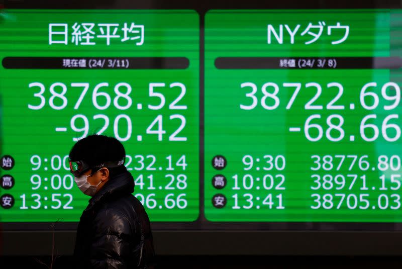 A passerby walks past an electric screen displaying Japan's Nikkei share average and the Dow Jones Industrial Average in Tokyo