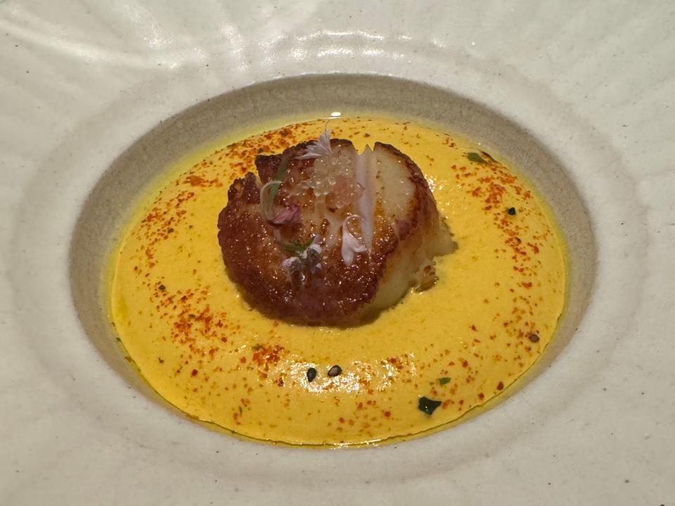 scallop and yellow sauce plated on a big saucer