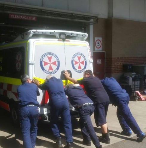 Five people push an ambulance into the Fairfield Workshop and mechanics.