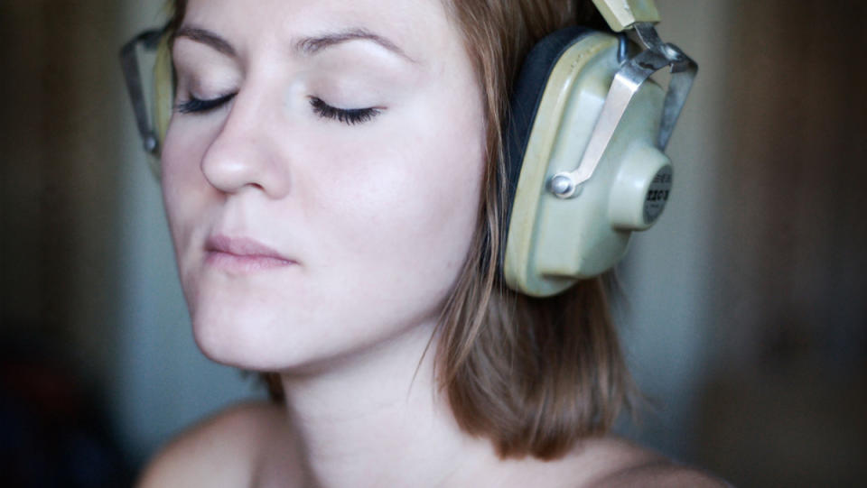 A woman with her eyes closed listens to music coming out of large, over-the-ear headphones.