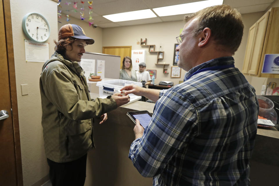 CORRECTS TO CAPITAL, NOT CAPITOL- In this Nov. 14, 2019 photo, Jon Combes, left, is given a bottle of buprenorphine, a prescription medicine that prevents withdrawal sickness in people trying to stop using opiates, by pharmacist Brad Livingstone, right, at the Olympia Bupe Clinic at the Capital Recovery Center, in Olympia, Wash. “They don’t care what your past is,” Combes said of the clinic’s staff. “They just want to get your future going.” (AP Photo/Ted S. Warren)