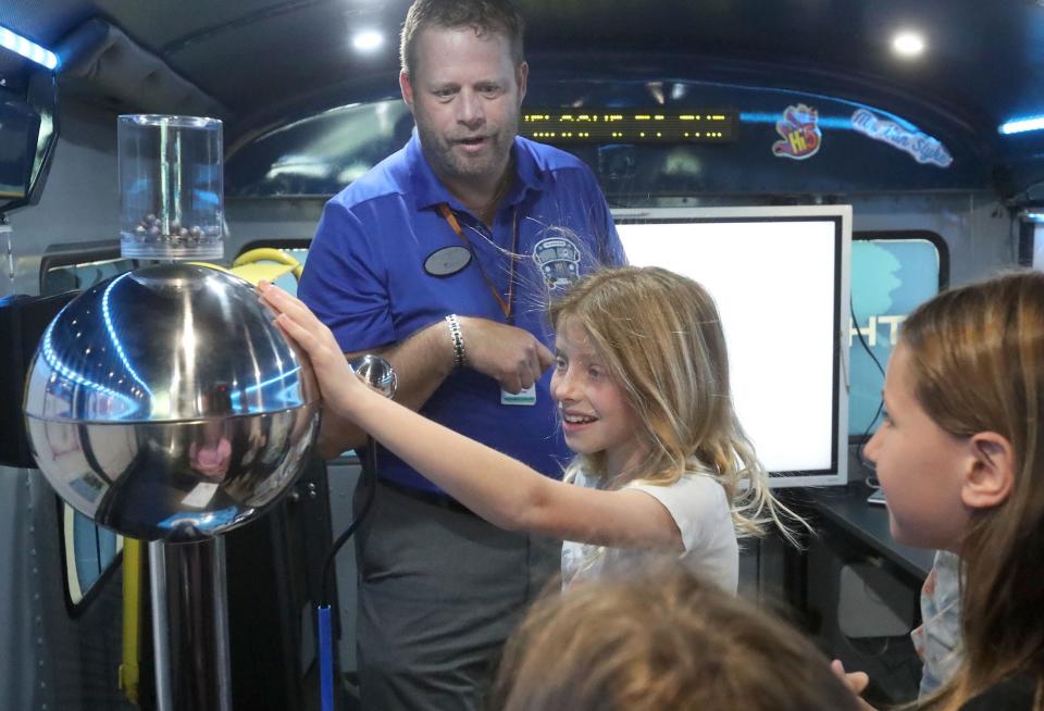 Beachside Elementary student Sienna Barrett smiles while touching the dome of the Van De Graff Generator as it makes her hair stand up, Tuesday, Oct. 3, 2023, as David Van Slyke, STEM bus resource teacher, gives the students a tour of Volusia County Schools' new STEM Bus.