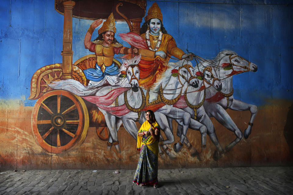 FILE - In this Sunday, May 12, 2019 file photo, an Indian woman displays the indelible ink mark on her finger after casting vote standing in front of a mural depicting a scene from the Hindu epic Mahabharata in Prayagraj, Uttar Pradesh state. The final phase of India’s marathon general election will be held on Sunday, May 19. The first of the election’s seven staggered phases was held on April 11. Vote counting is scheduled to start on May 23. India has 900 million eligible voters. (AP Photo/Rajesh Kumar Singh, File)