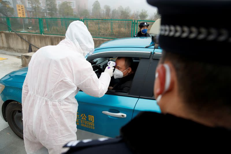 A medical worker in protective suit checks the body temperature of a driver at a checkpoint outside the city of Yueyang