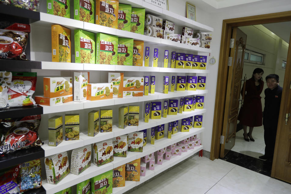 In this March 13, 2019, photo, employees peek through a door into a showroom at a food factory in Pyongyang, North Korea. North Korean factories are filling city store shelves with ever better and fancier snack foods and sugary drinks, while government officials and international aid organizations warn the nation could be on the verge of a major food crisis. (AP Photo/Dita Alangkara)