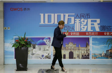 FILE PHOTO: A man stands next to a poster of immigration agency Qiaowai Group at the lobby to its office, in Beijing, China May 10, 2017. REUTERS/Jason Lee/File Photo