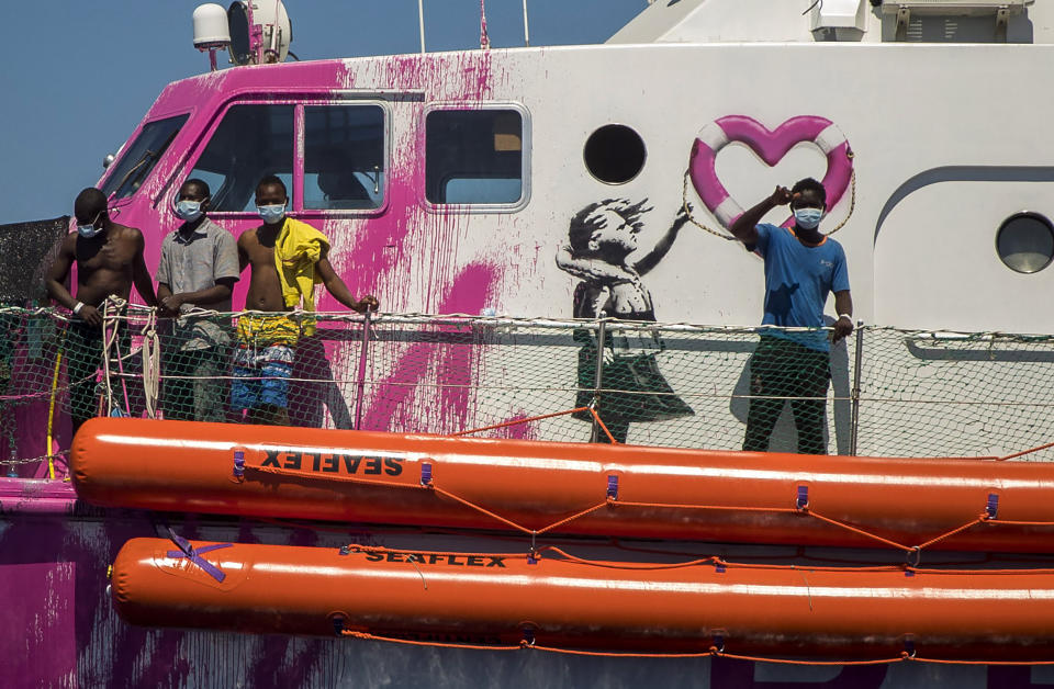 A boy waves to the crew of the Astral rescue vessel from the deck of the Louise Michel rescue vessel, a French patrol boat currently manned by activists and funded by the renowned artist Banksy in the Central Mediterranean sea, at 50 miles south from Lampedusa, Friday, Aug. 28, 2020. A Berlin-based group says it has begun migrant rescue operations in the Mediterranean Sea with a bright pink former navy vessel sponsored by British artist Banksy. The group operating the MV Louise Michel, a sleek 30-meter (98-foot) ship named after a 19th century French feminist and anarchist, said late Thursday that it rescued 89 from an inflatable boat in distress. (AP Photo/Santi Palacios)