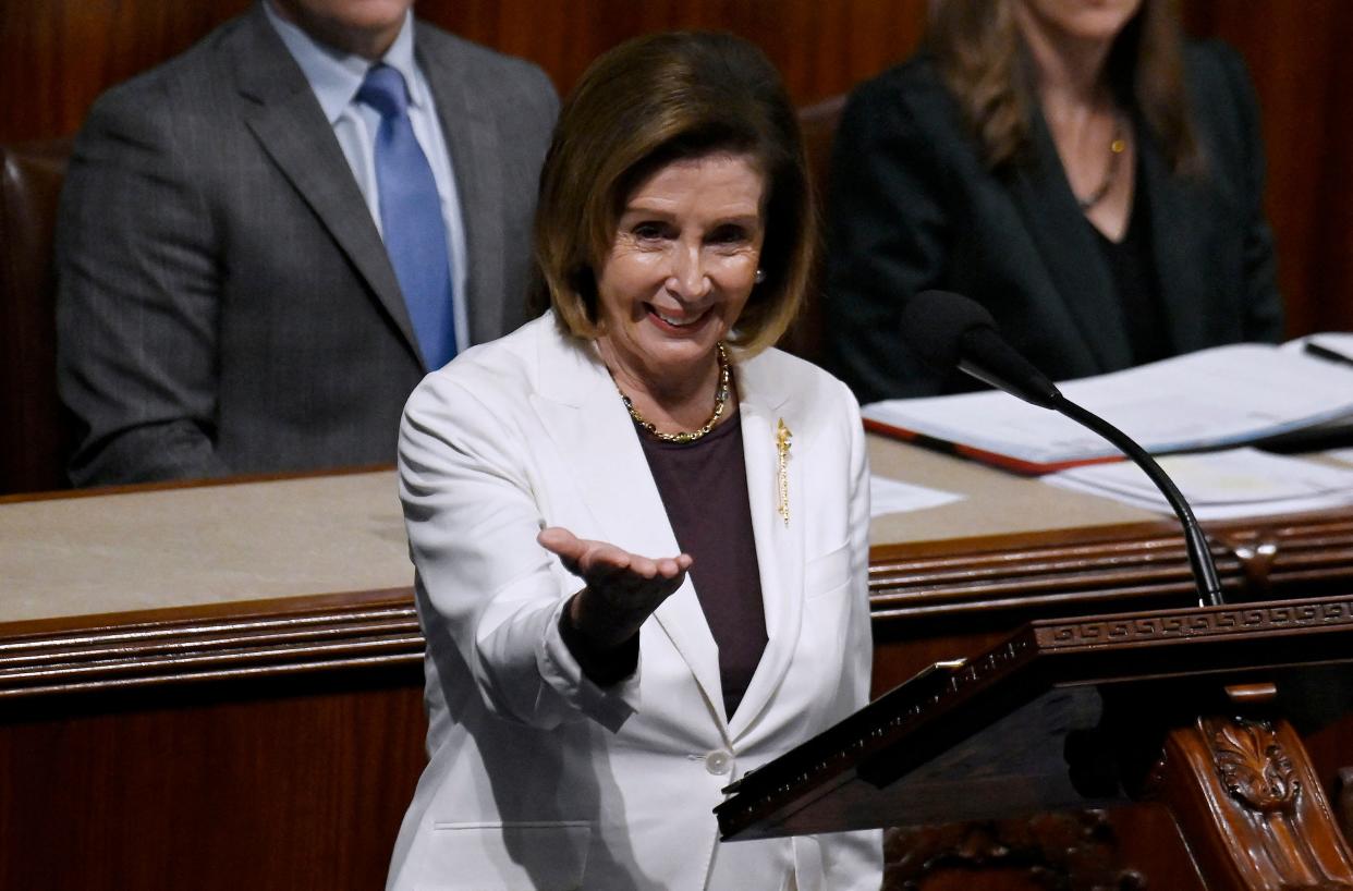 Nancy Pelosi, at the microphone, acknowledges her audience in a gesture of appreciation.