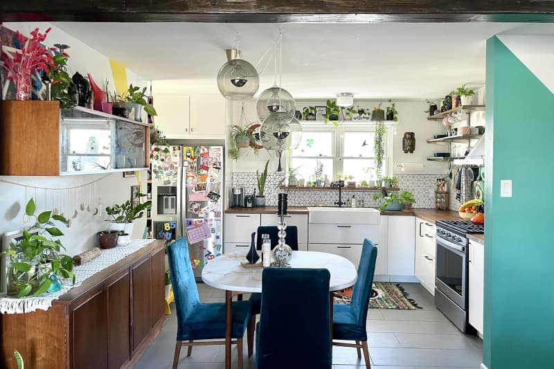 white kitchen with lots of plants, bold color paint details, and dining table with blue chairs