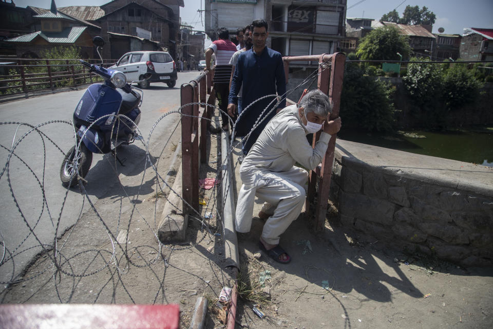 CORRECTS AGE - Kashmiri civilians cross a barricade set up by the police in Srinagar, Indian controlled Kashmir, Thursday, Sept. 2, 2021. Indian authorities cracked down on public movement and imposed a near-total communications blackout Thursday in disputed Kashmir after the death of Syed Ali Geelani, a top separatist leader who became the emblem of the region’s defiance against New Delhi. Geelani, who died late Wednesday at age 91, was buried in a quiet funeral organized by authorities under harsh restrictions, his son Naseem Geelani told The Associated Press. He said the family had planned the burial at the main martyrs’ graveyard in Srinagar, the region’s main city, as per his will but were disallowed by police. (AP Photo/ Mukhtar Khan)