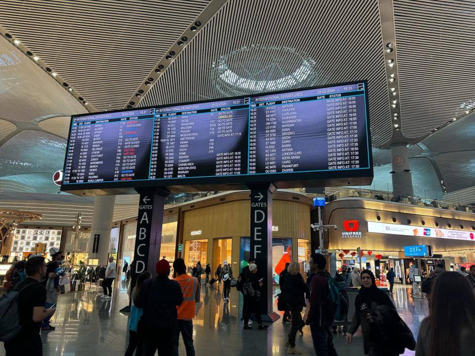 People walking under an international-departures board in an airport.