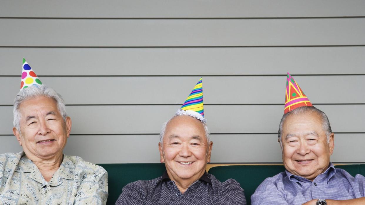 portrait of three elderly men sitting on couch wearing birthday hats