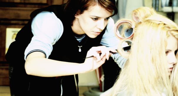 Female hairdresser adjusting curlers in a mid adult woman's hair