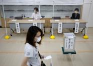 Members of Election Management Committee wearing protective face masks are seen through plastic curtains amid the coronavirus disease (COVID-19) outbreak, at a voting station for the Tokyo Governor election in Tokyo