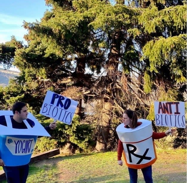 a man wearing a cardboard yogurt and and holding a probiotics sign with a woman wearing a cardboard pill bottle and holding an antbiotics sign