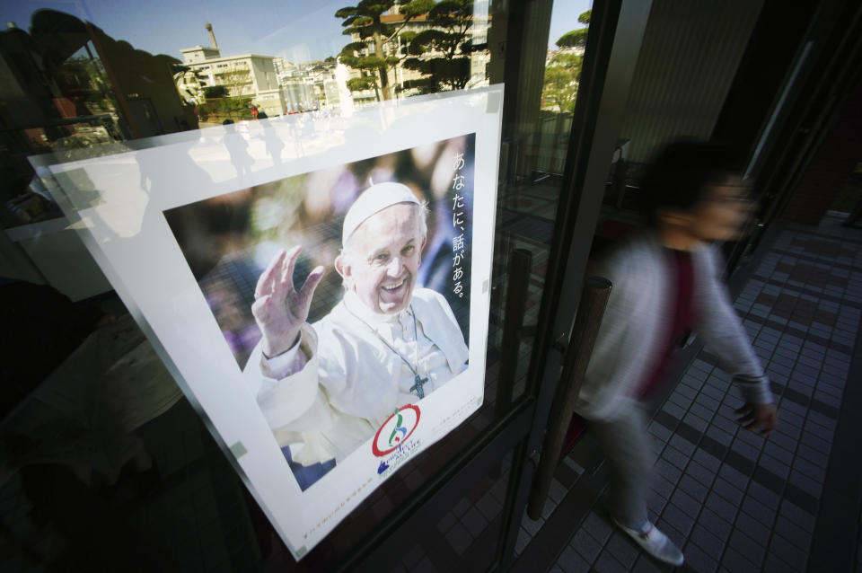 In this Nov. 16, 2019, photo, a woman walks by a poster of Pope Francis at the Urakami Cathedral in Nagasaki, southern Japan. Pope Francis will start his first official visit to Japan in Nagasaki, ground zero for the Christian experience in a nation where the Catholic leader once dreamed of living as a missionary. (AP Photo/Eugene Hoshiko)