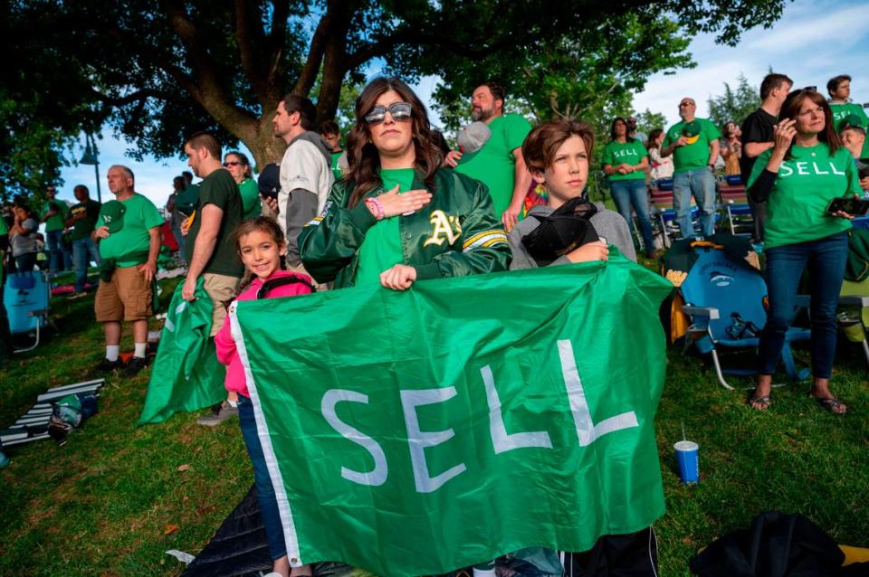 A’s fan Kristen Cutberth of Roseville holds a “SELL” flag with her children Lucy, 7, left, and Logan, 10, during a protest Saturday at the River Cats-Aviators game.