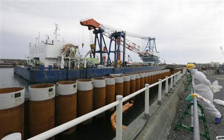 A Tokyo Electric Power Co. (TEPCO) employee wearing a protective suit and mask stands next to an impervious wall made of a steel pipe sheet pile installed along the coast, facing nuclear reactor buildings No. 1 to No. 4, at the tsunami-crippled TEPCO's Fukushima Daiichi nuclear power plant in Fukushima prefecture, November 7, 2013. REUTERS/Kimimasa Mayama/Pool