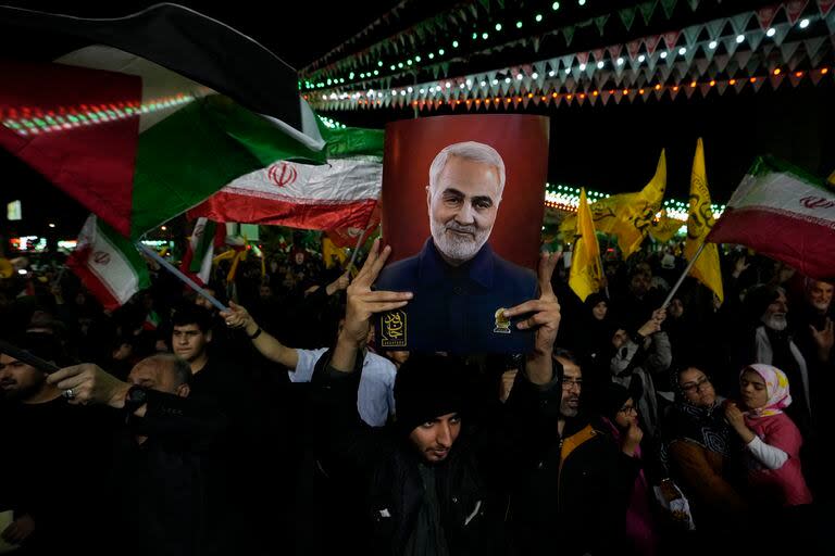 Manifestantes ondean banderas iraníes y palestinas mientras uno de ellos sostiene un cartel con al imagen del fallecido general de la Guardia Revolucionaria Iraní Qassem Soleimani, asesinado en un ataque estadounidense en 2020 durante su manifestación contra Israel para condenar la muerte de miembros de la Guardia Revolucionaria en Siria, en la plaza Felestin de Teherán, el 1 de abril de 2024. (AP Foto/Vahid Salemi)