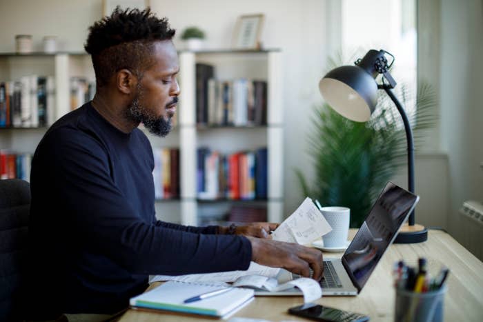 Man at desk reviewing papers, with a lamp and computer, in a home office setting