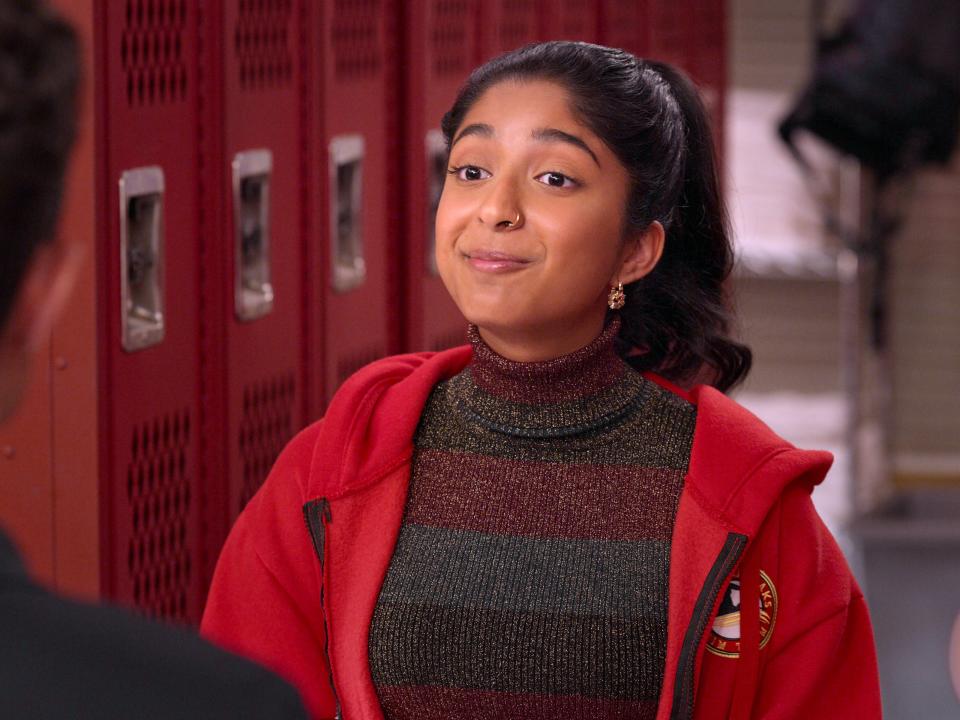 devi in never have i ever, smiling optimistically and wearing a red jacket