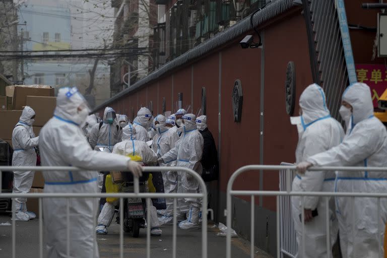 Como en los peores de la pandemia, trabajadores enfundados en trajes protectores aguardan para cumplir con sus tareas en Pekín