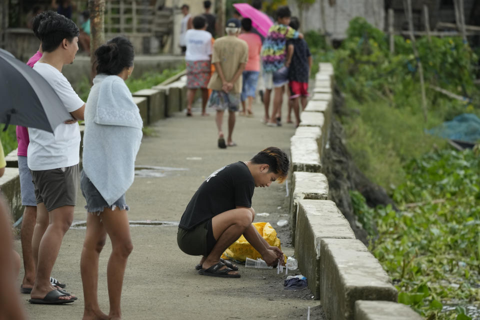 A resident lights candles along the coastal village of Kalinawan where a passenger boat capsized in Binangonan, Rizal province, Philippines on, Friday, July 28, 2023. A small Philippine ferry turned upside down when passengers suddenly crowded to one side in panic as fierce winds pummeled the wooden vessel, leaving scores of people dead while others were rescued, officials said Friday. (AP Photo/Aaron Favila)