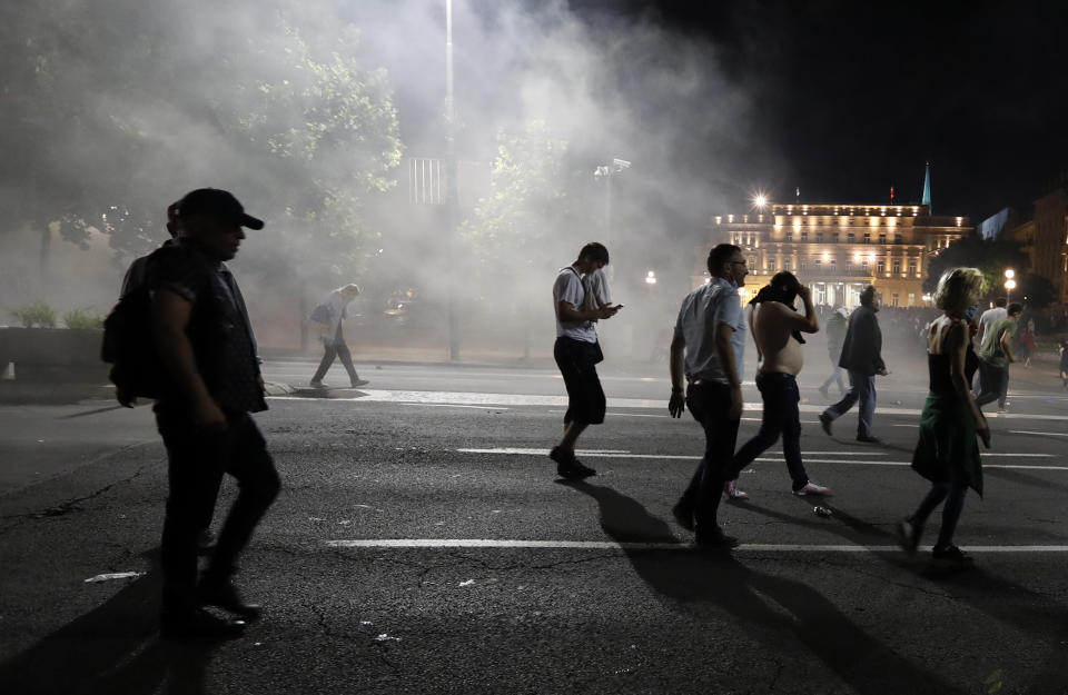 Protesters run from tear gas in front of the Serbian parliament building in Belgrade, Serbia, Tuesday, July 7, 2020. Thousands of people protested the Serbian president's announcement that a lockdown will be reintroduced after the Balkan country reported its highest single-day death toll from the coronavirus Tuesday. (AP Photo/Darko Vojinovic)